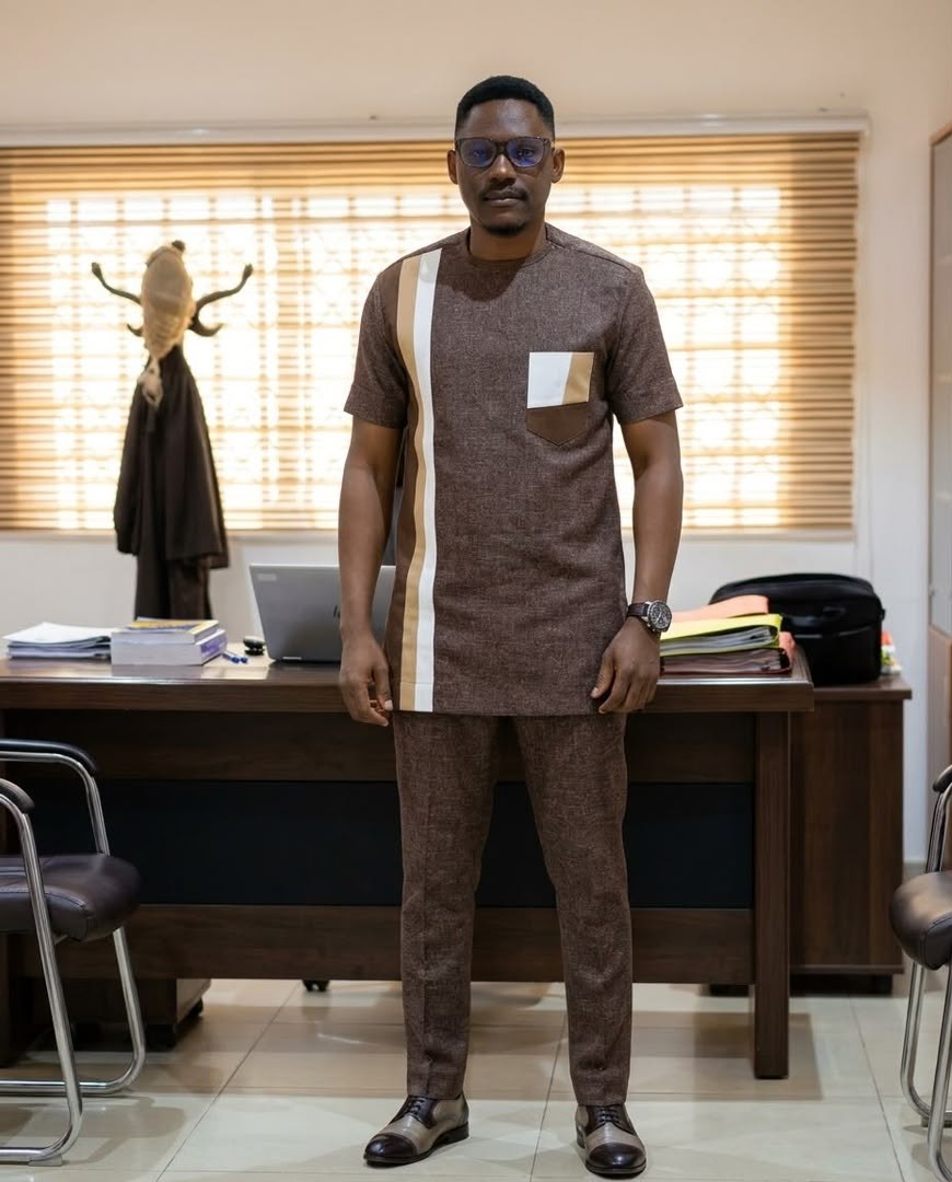Man in the Luxury Dotse Set, a brown textured two-piece kaftan with a cream stripe and contrast chest pocket, standing in an office